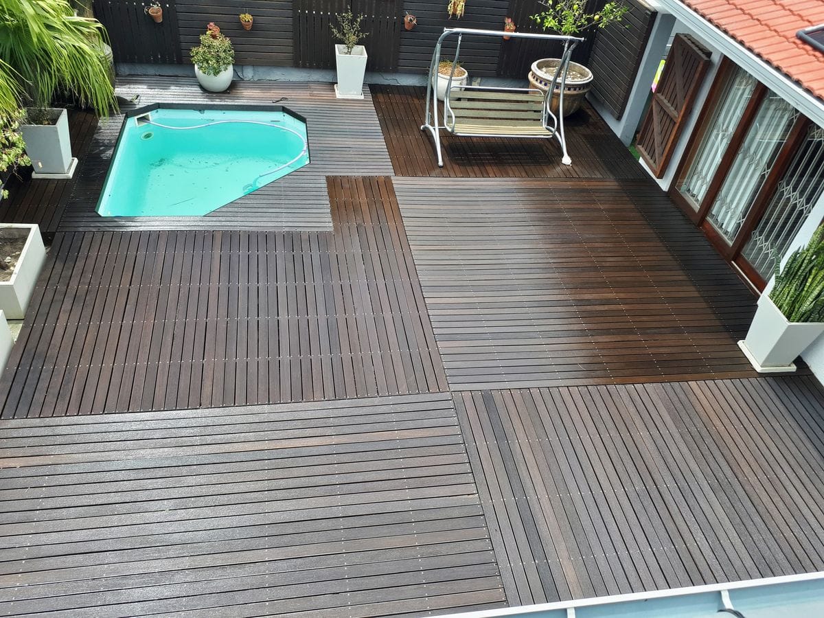 Varnished timber pool deck in Strand, seen from above, with a swing bench and potted plants