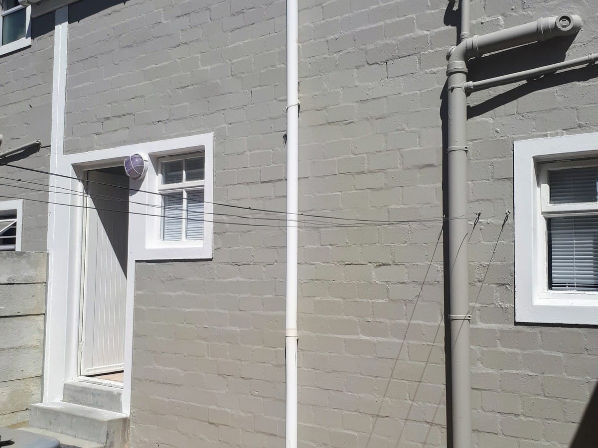 Exterior brick wall and window frames in Strand, repainted in grey with white trim
