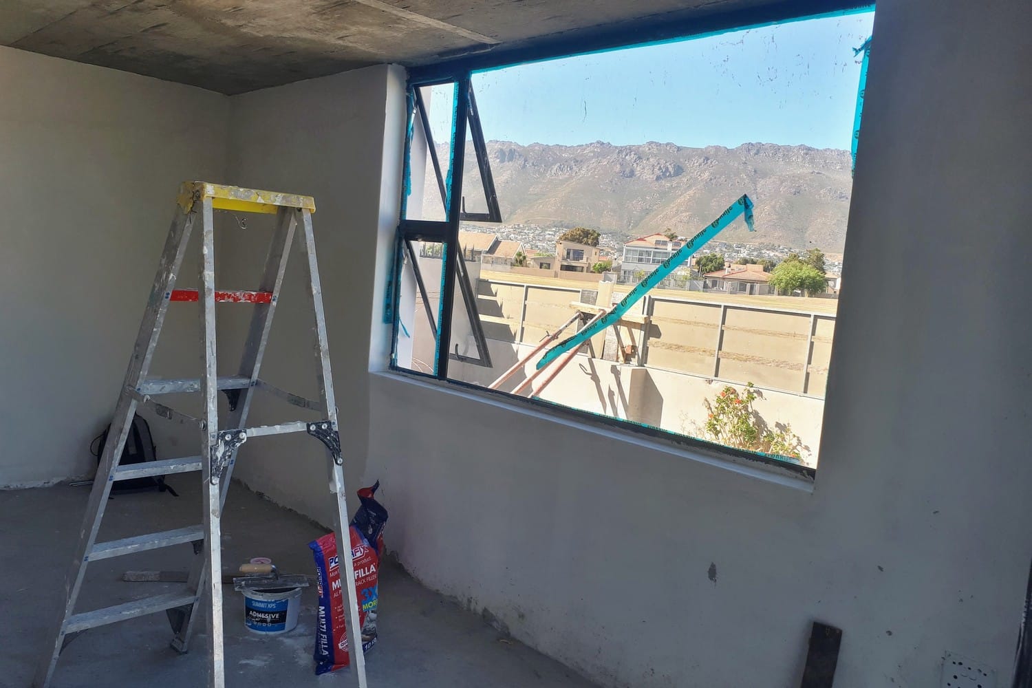 Unpainted new-build room in Gordon's Bay with bare plaster walls and a stepladder