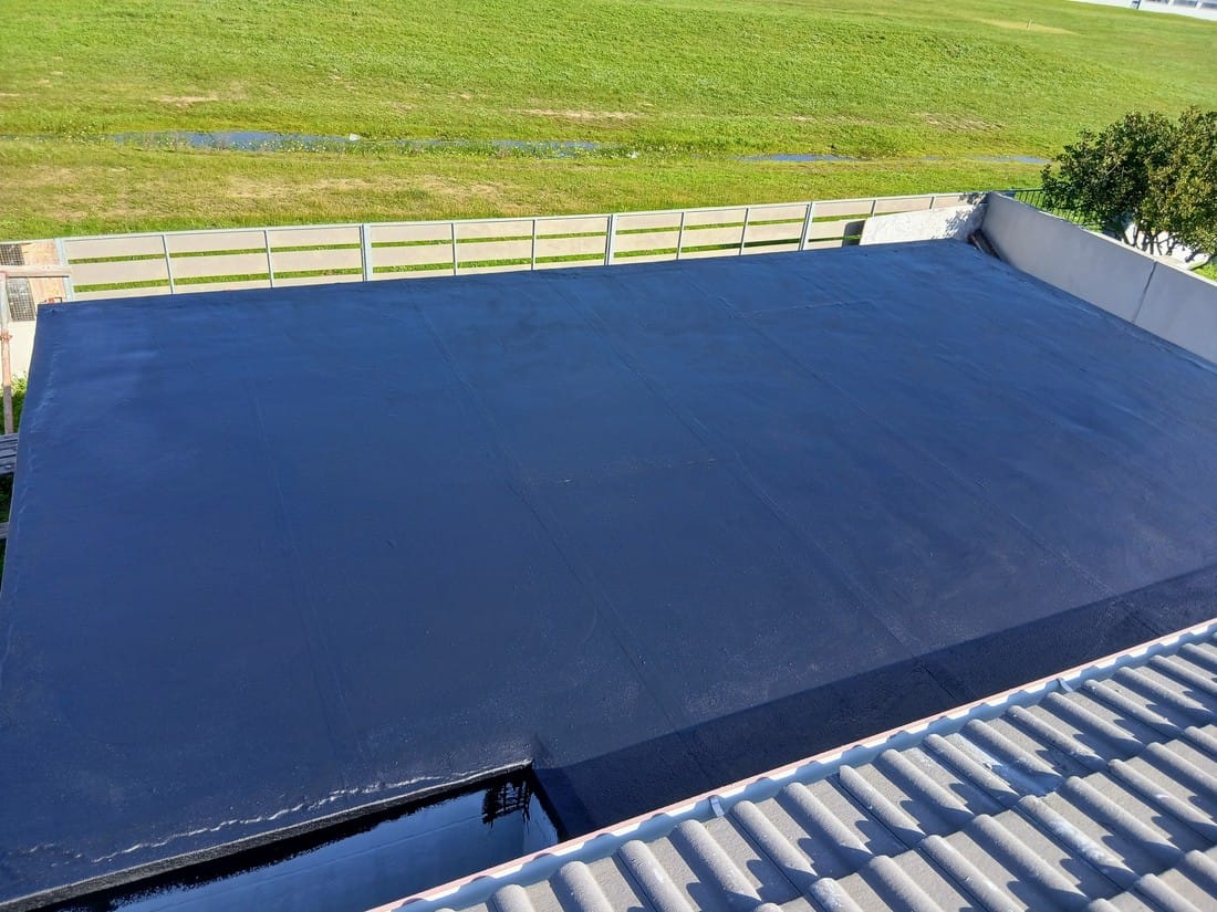 Flat roof waterproofed with a dark blue coating, seen from above next to open grassland