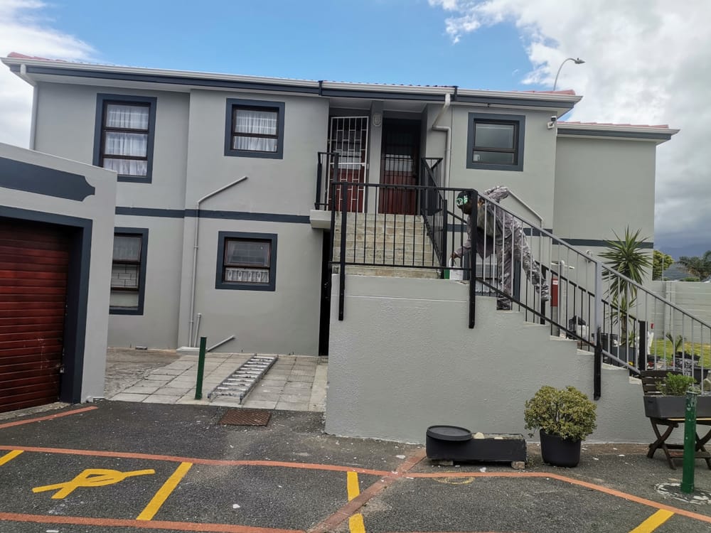 Exterior of a two-storey residential building repainted with dark blue window trim, painter working on the staircase